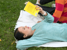 Tyttö lukee kirjaa puistossa piknik-peiton päällä.