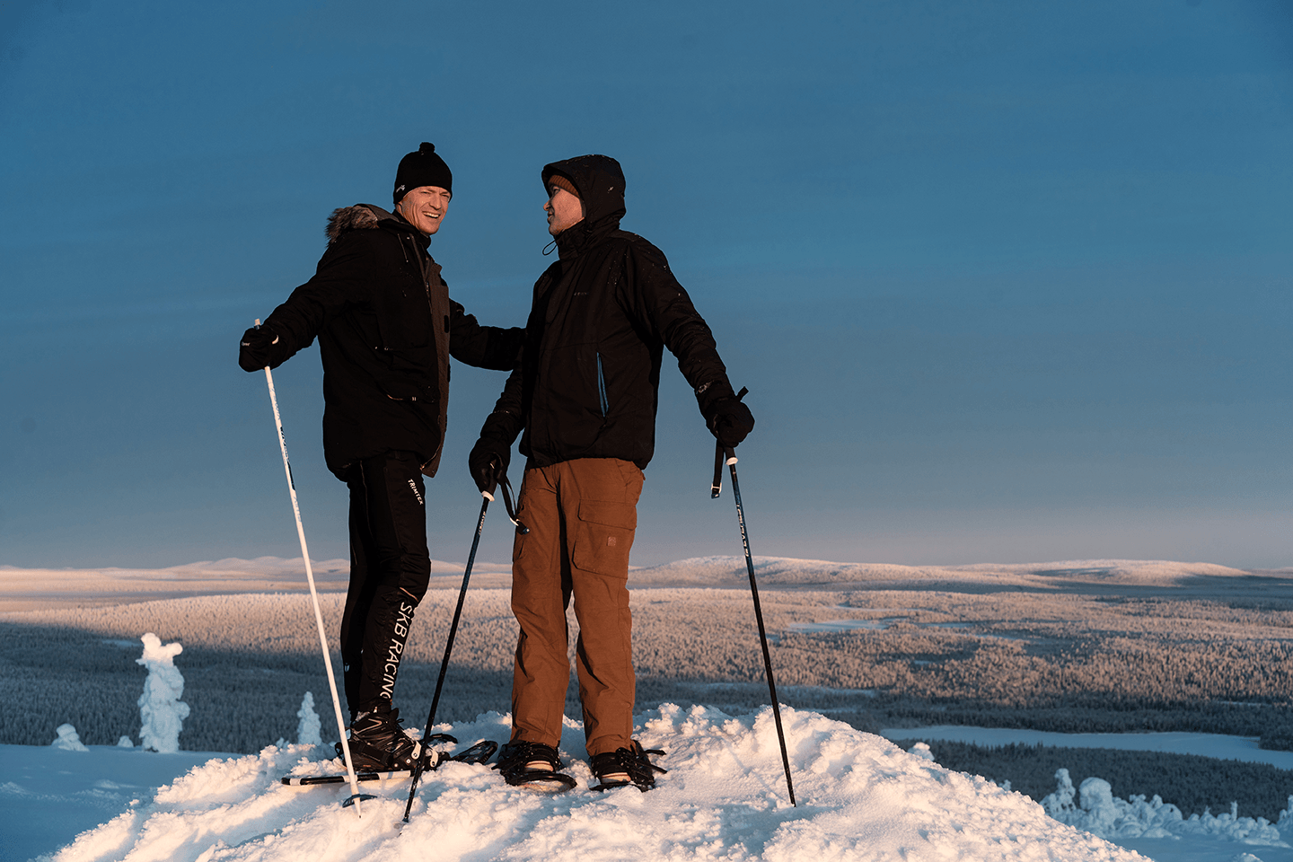 Kaksi miestä hiihtää ja hymyilee.