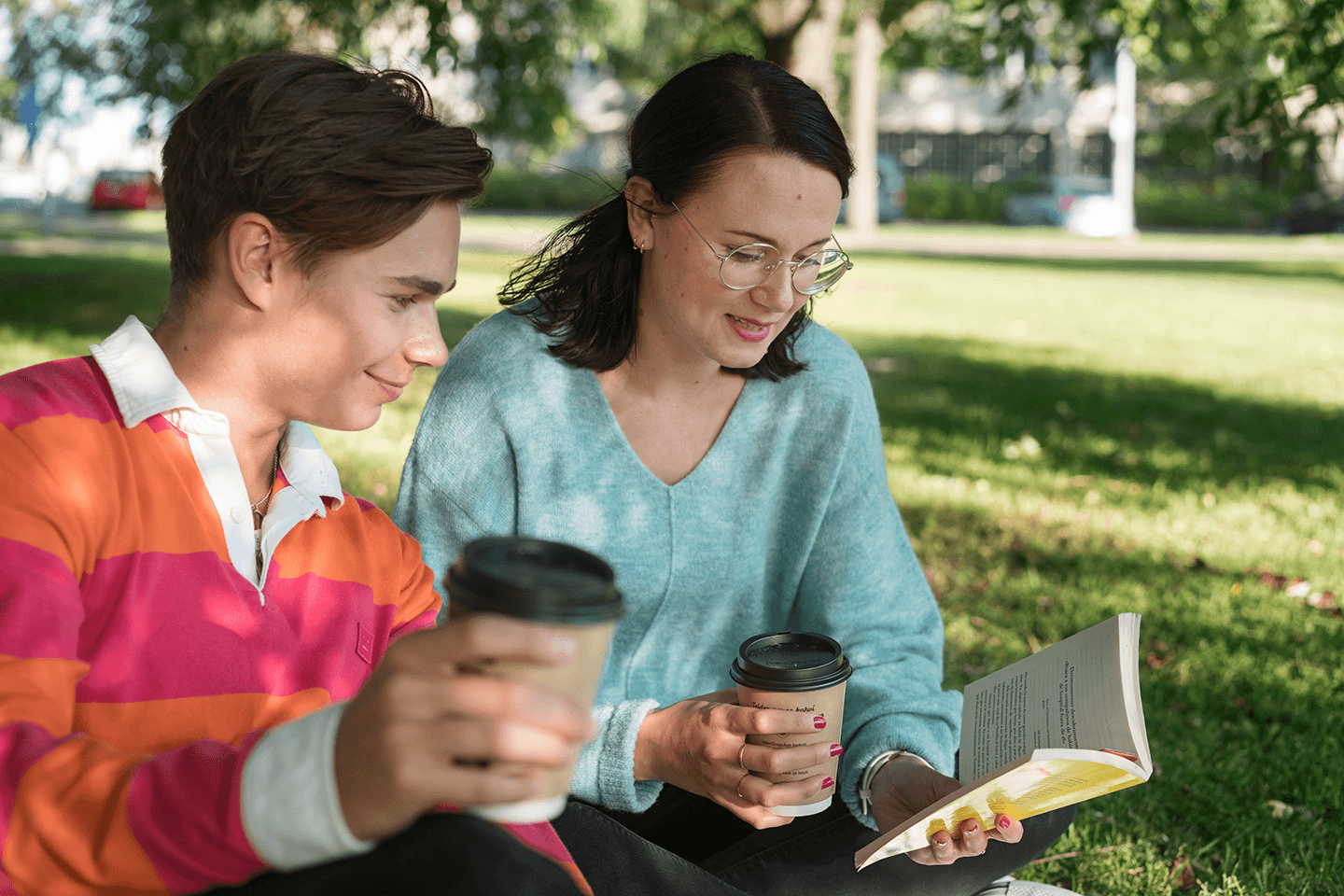 Nuori poika ja työttö istuvat puistossa juomassa kahvia ja lukemassa.