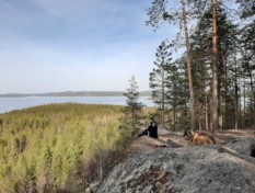 Järvimaisema kalliolta, nainen ja kaksi koiraa.