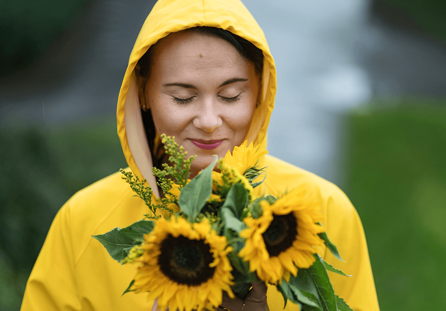 Nainen keltaisessa sadetakissa pitelee auringonkukkia.
