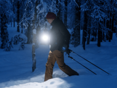 A person skiing in the dark with a lamp.