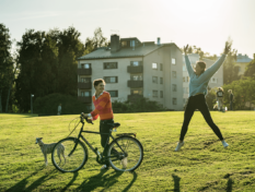 Man jumps up in the air and a woman holds a bicycle.