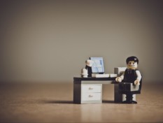 Legoukko istuu yksin toimistopöydän ääressä ja irvistää.