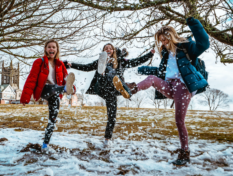 Kolme nuortapotkii iloisena sohjoista lunta.
