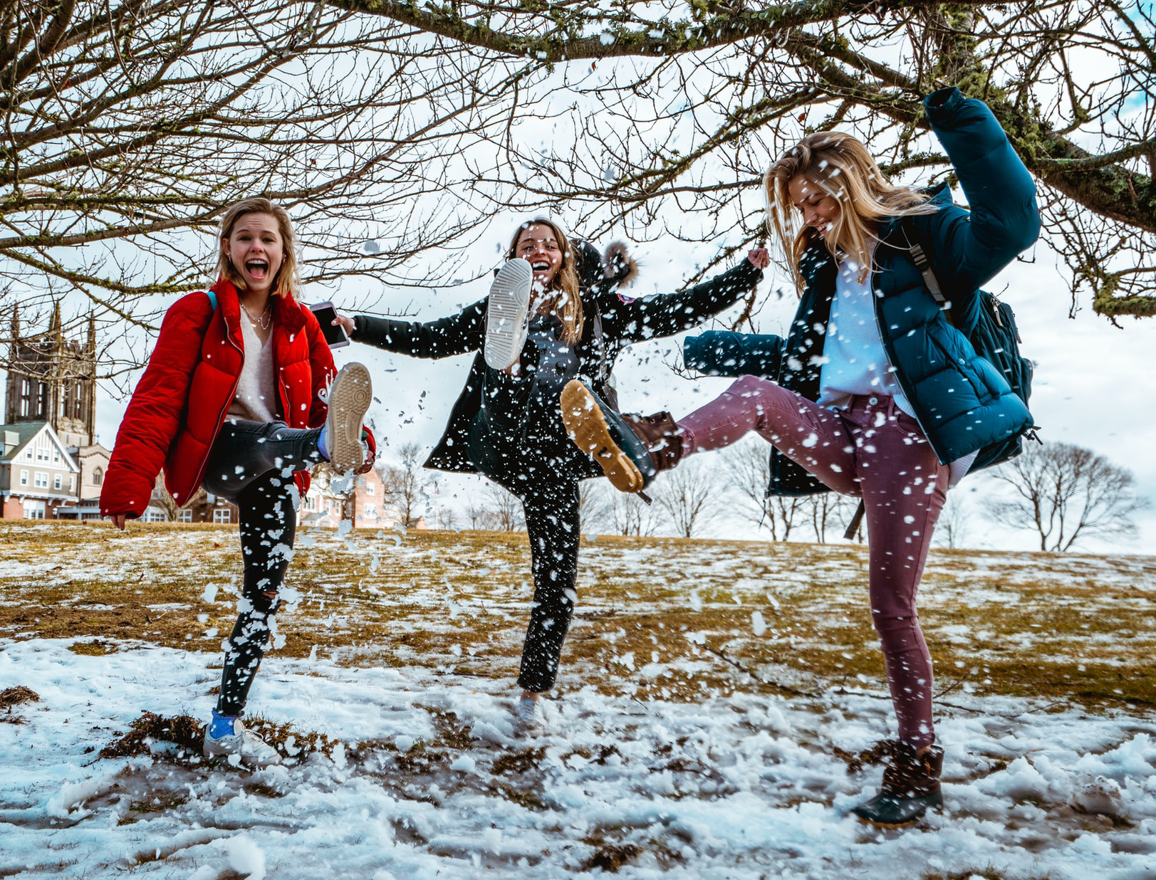 Kolme nuortapotkii iloisena sohjoista lunta.