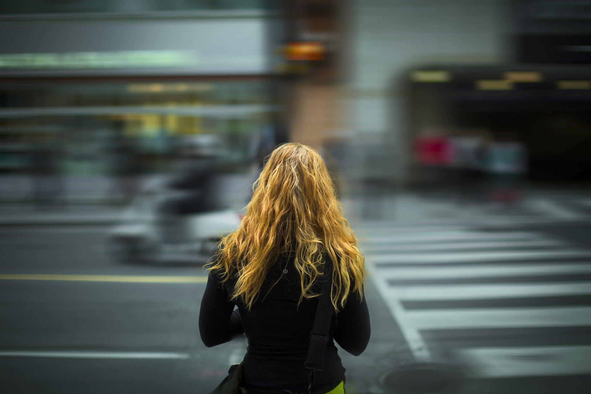 Kuvassa nuori nainen seisoo vilkkaasti liikennöidyn kadun varrella.