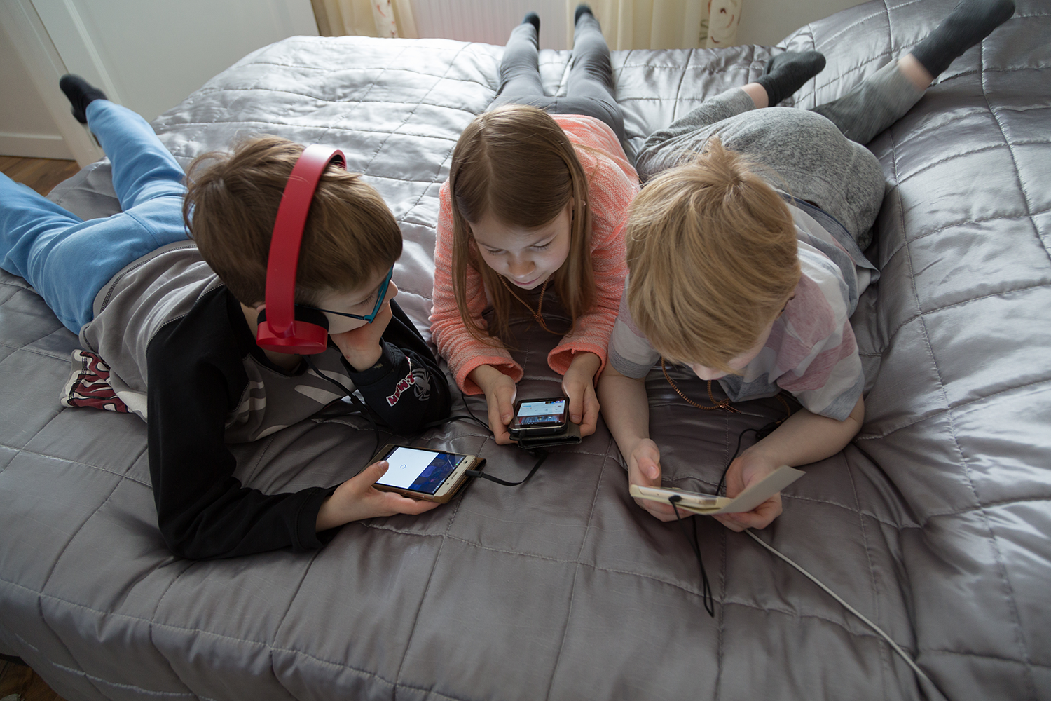 Kolme lasta katsoo puhelimieen sängyllä.