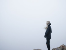 En ung person står på ett berg och ser en dimmig vy.