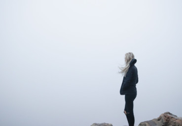 En ung person står på ett berg och ser en dimmig vy.