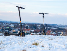 Kaksi sähköpotkulautaa pysäköitynä lumisella mäellä.