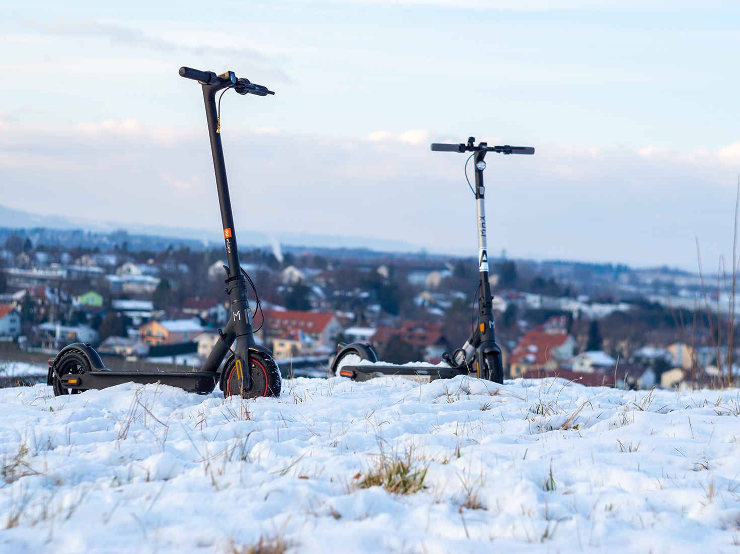 Kaksi sähköpotkulautaa pysäköitynä lumisella mäellä.