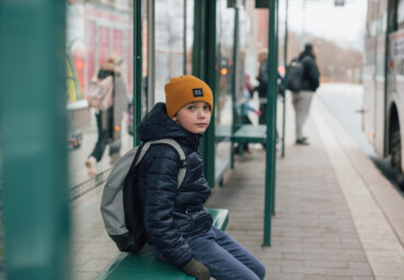Ett barn sitter ensam på en busshållplats och väntar på buss.