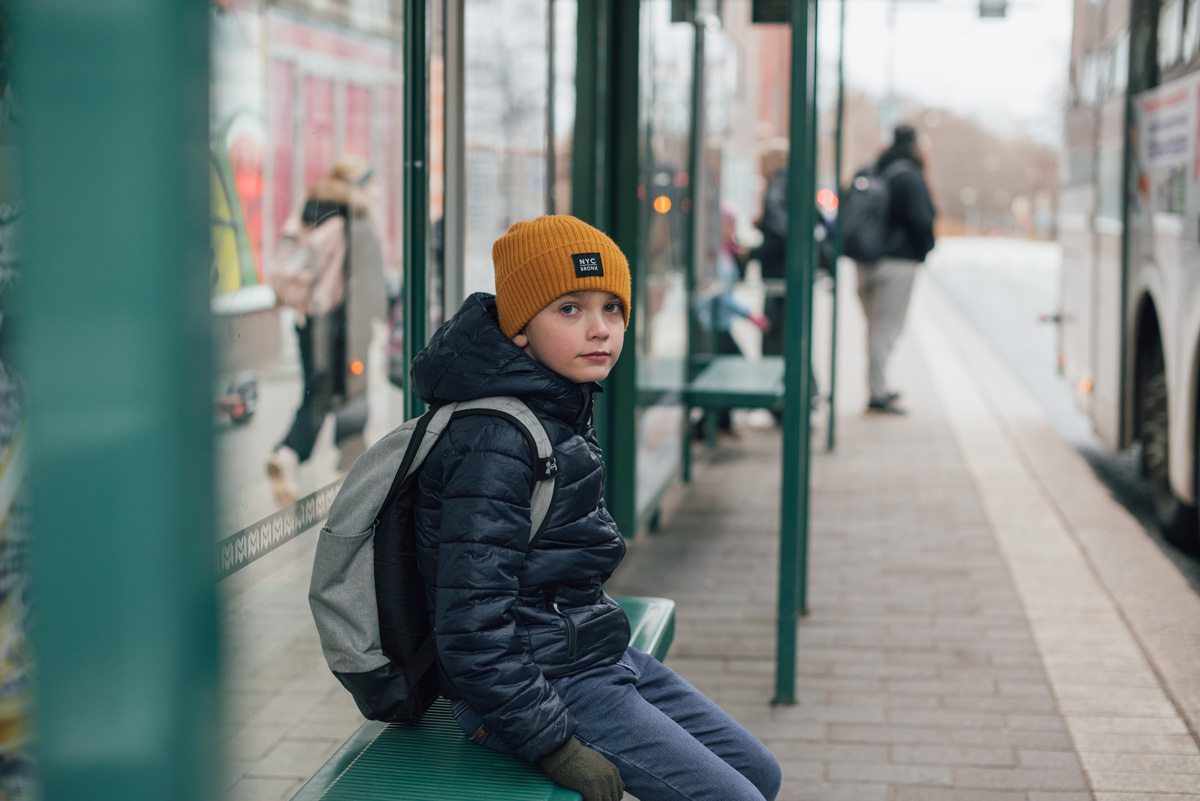 Ett barn sitter ensam på en busshållplats och väntar på buss.