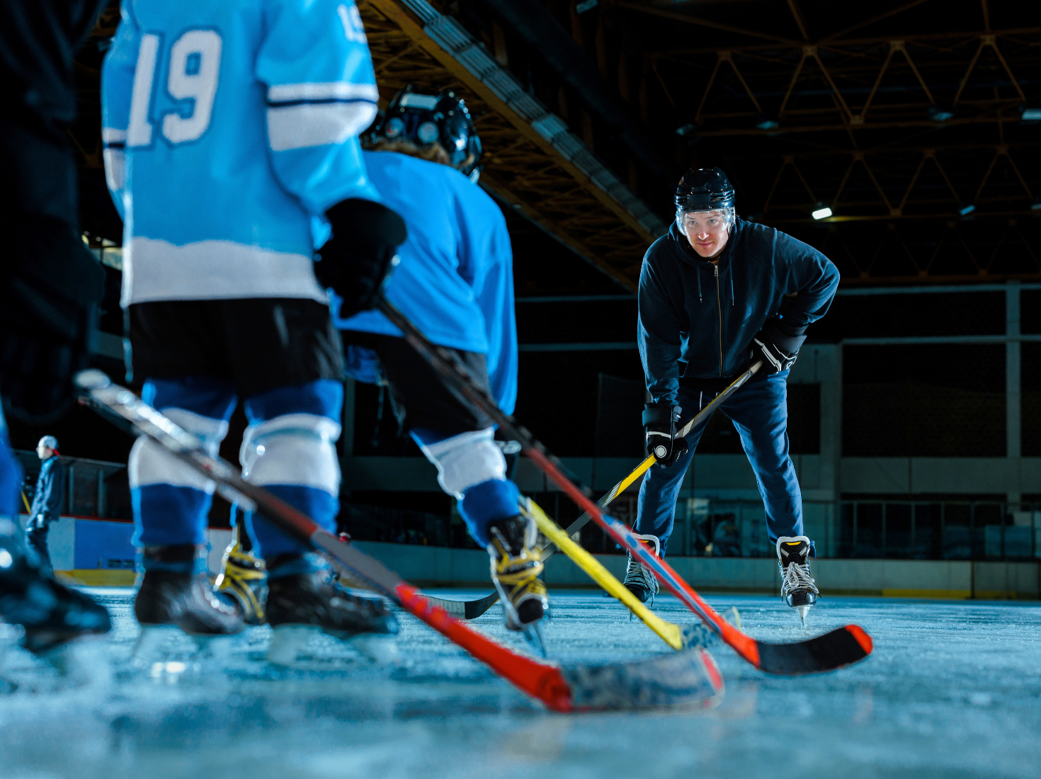 Jääkiekkokaukalossa aikuinen ohjaamassa nuorten jääkiekkoilijoiden pelaamista.