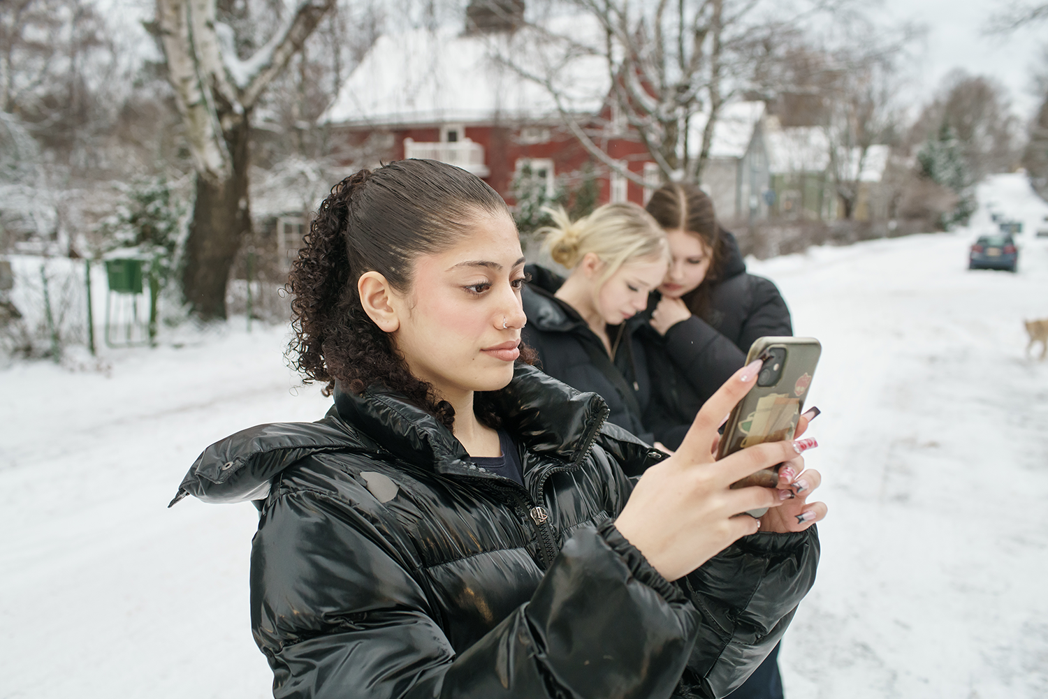 Kolme nuorta katsoo puhelimiaan talvisäässä.
