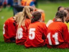 Tyttöjen jalkapallojoukkue istuu kentällä.