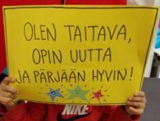 apsi pitää kylttiä, jossa lukee: Olen taitava, opin uutta ja pärjään hyvin.
