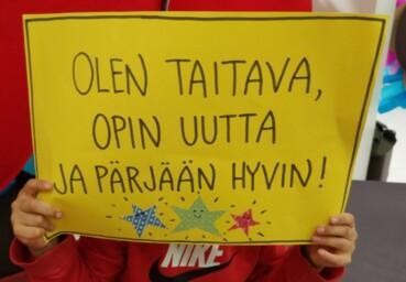 apsi pitää kylttiä, jossa lukee: Olen taitava, opin uutta ja pärjään hyvin.