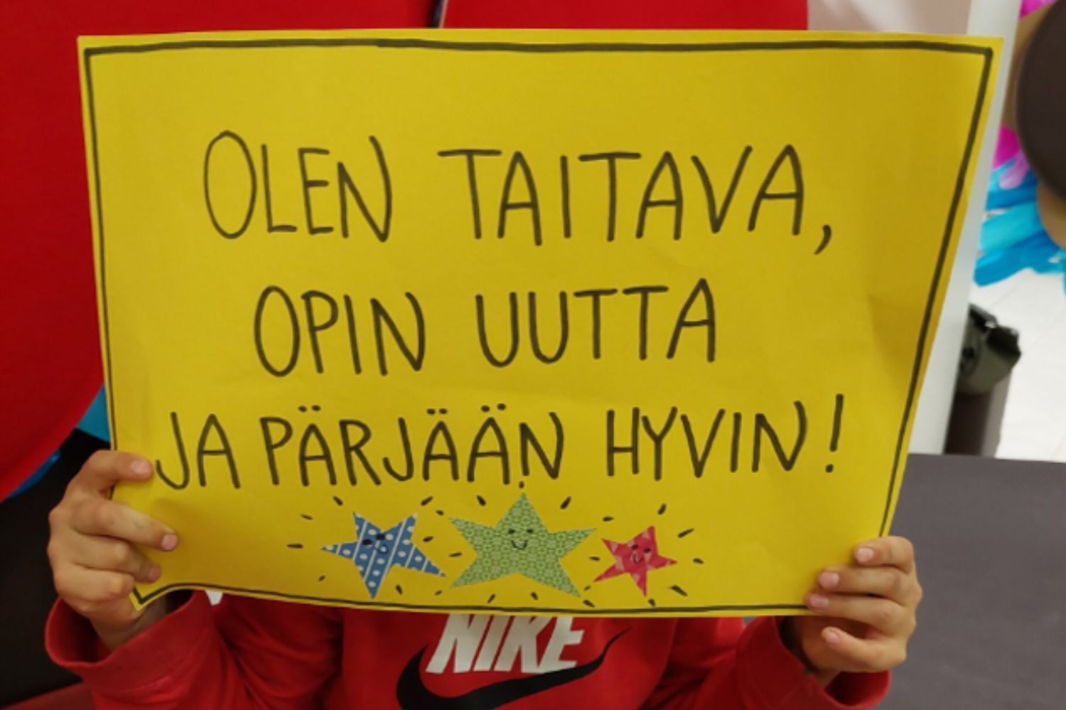 apsi pitää kylttiä, jossa lukee: Olen taitava, opin uutta ja pärjään hyvin.